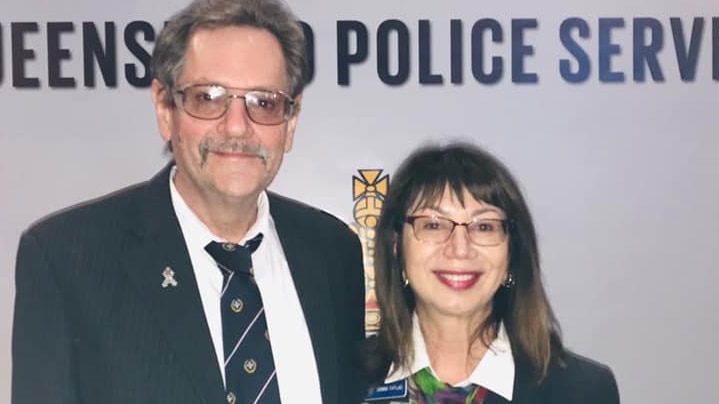 a man and a woman stand next to each other smiling at the camera in front of a queensland police service banner