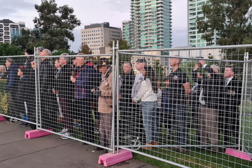 A crowd watches the Anzac Day dawn service from behind a temporary fence.