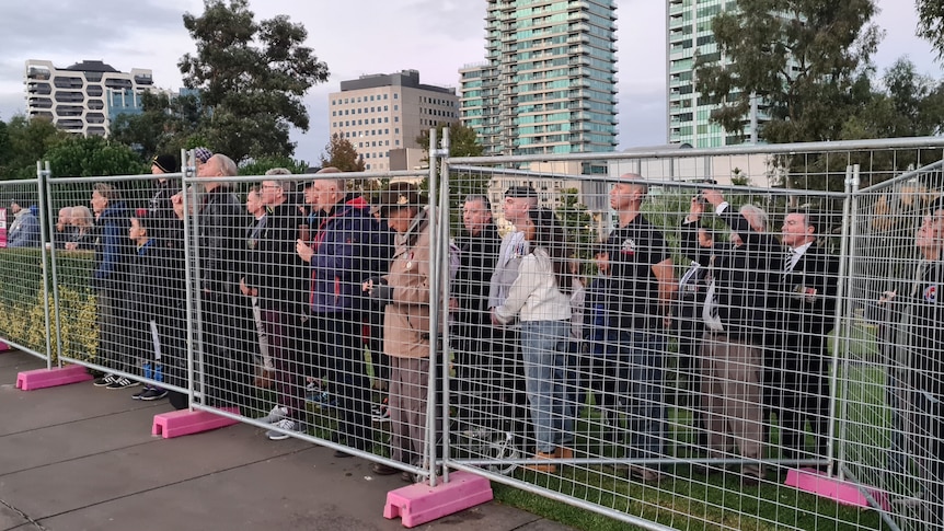 A crowd watches the Anzac Day dawn service from behind a temporary fence.