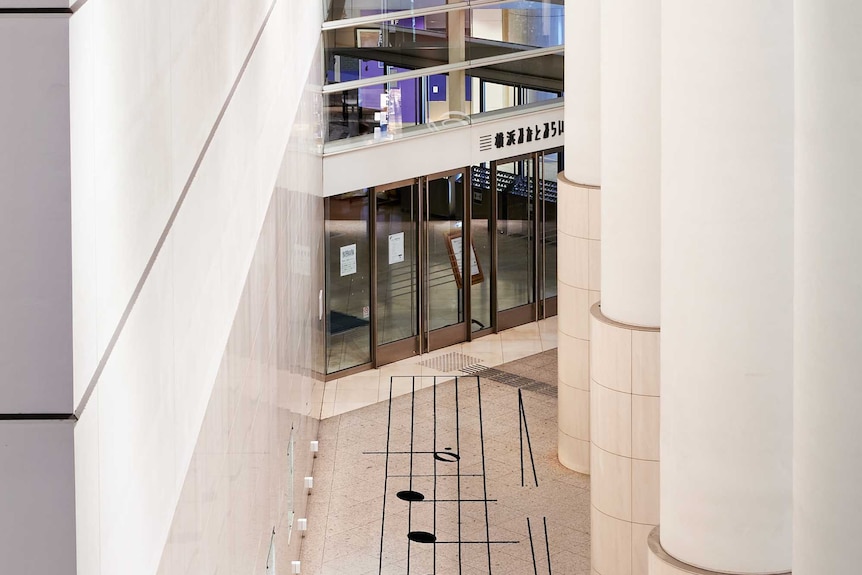 Aerial photograph of the first phrase of Satie's Gymnopédie No. 1 printed on the floor of a large atrium, leading to a door.