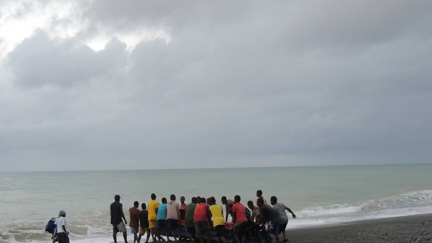 A larger group of Solomon Islanders pushing a boat into the ocean