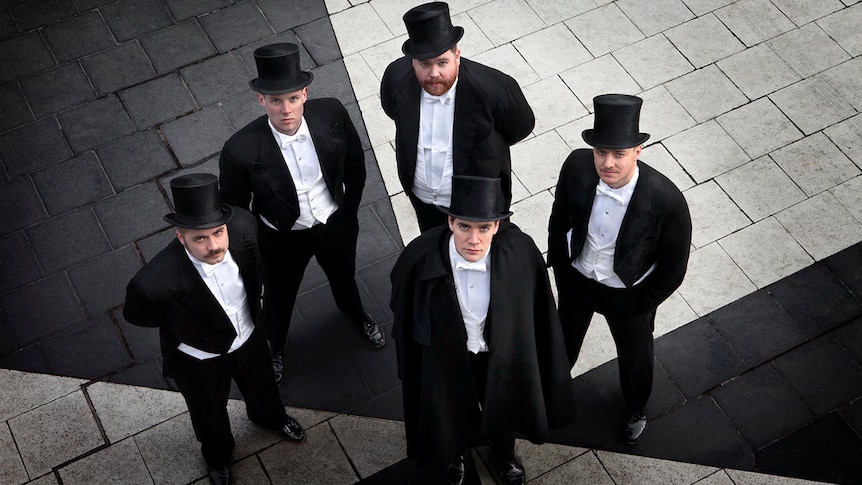 Five members of The Hives wearing matching suits with top hats and tails