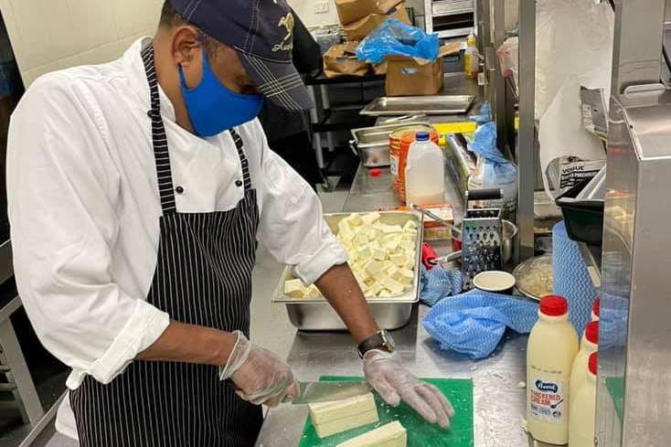 Una persona che indossa una maschera taglia il tofu in cucina.