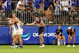 A Fremantle AFL player shouts and gesticulates as two North Melbourne teammates hug after the final siren in a game.