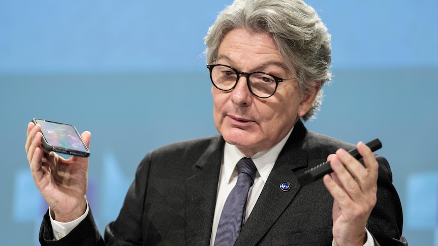 Thierry Breton speaks during a media conference holding two smartphones