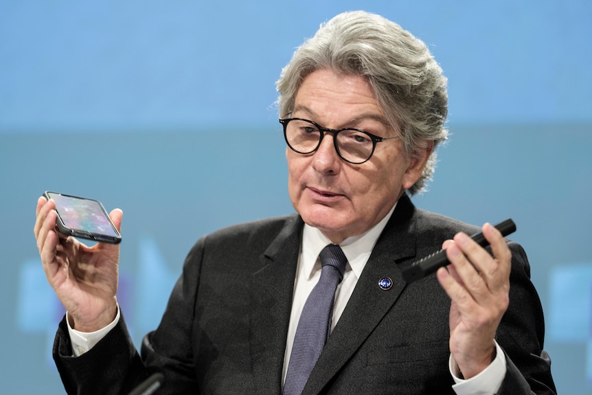 Thierry Breton speaks during a media conference holding two smartphones