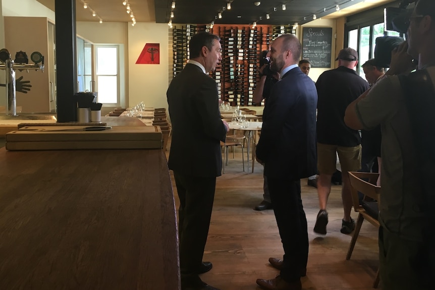 Two men in suits talk near a restaurant bar.