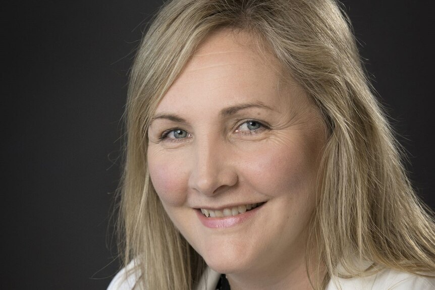 A smiling, blonde woman against a black background.