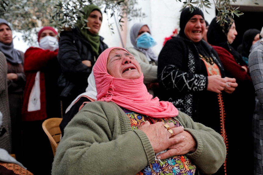 A woman in a pink headscarf grips her chest and sobs at a funeral