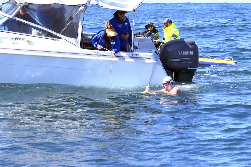 A man in the ocean is about the take a drink floated to him by a support crew member.