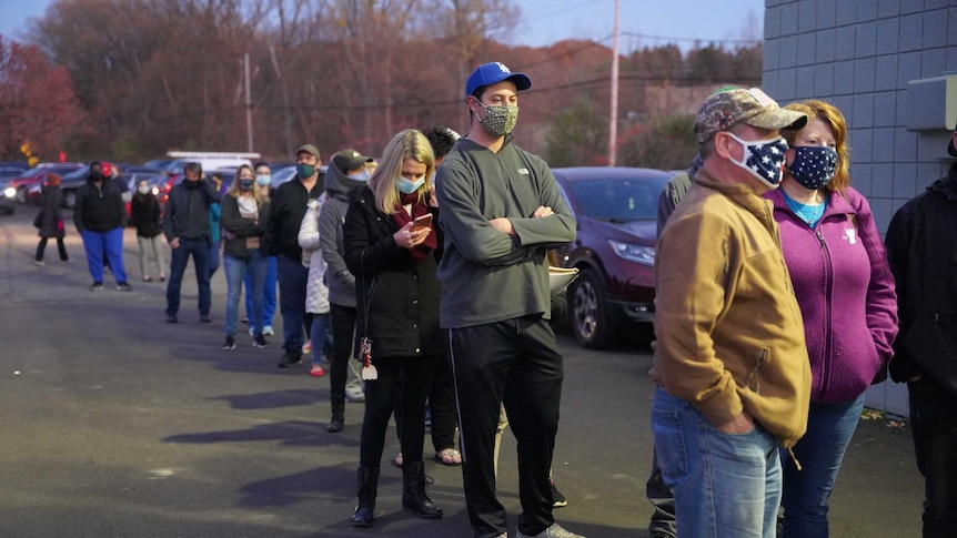 A group of people wearing masks stand in line along a road.