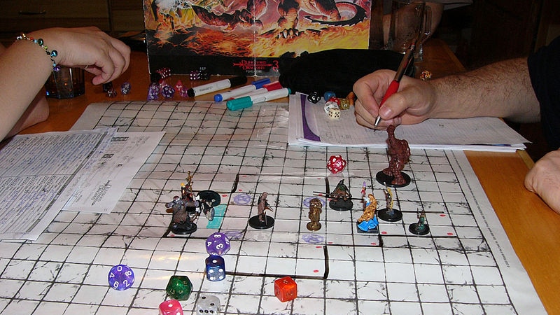 A game of Dungeons and Dragons is underway: miniature fighters and dice adorn a grid laid out on a table.