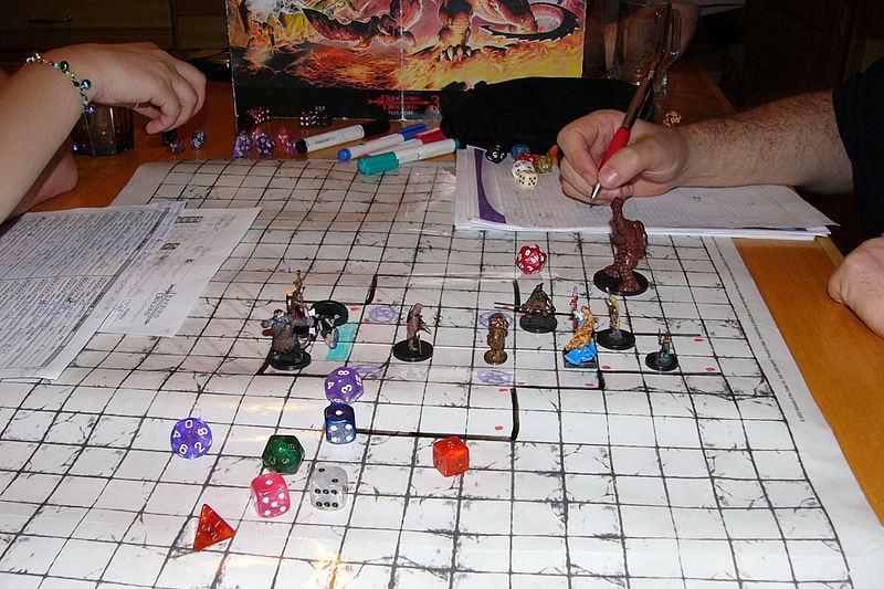 A game of Dungeons and Dragons is underway: miniature fighters and dice adorn a grid laid out on a table.