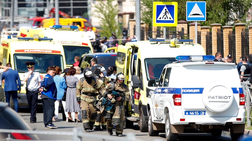 Firefighters walk past ambulances and police cars and a truck parked at a school after a shooting in Kazan, Russia.