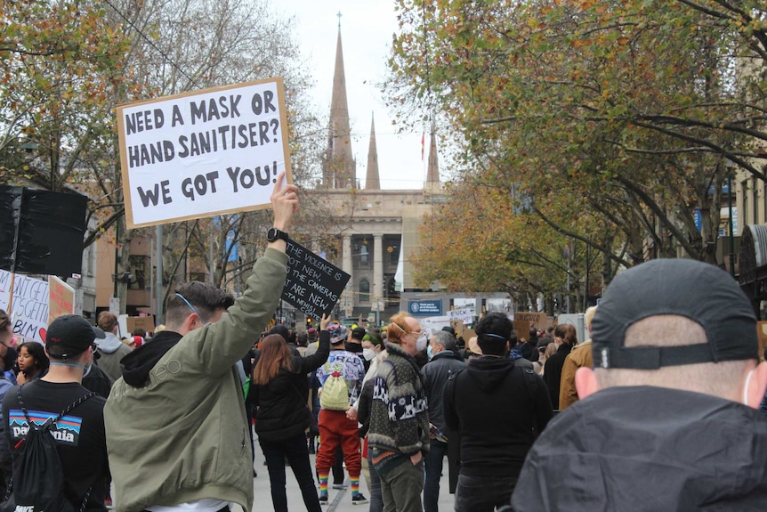 A protester holds up a sign saying 'need a mask or hand sanitiser? We got you!'