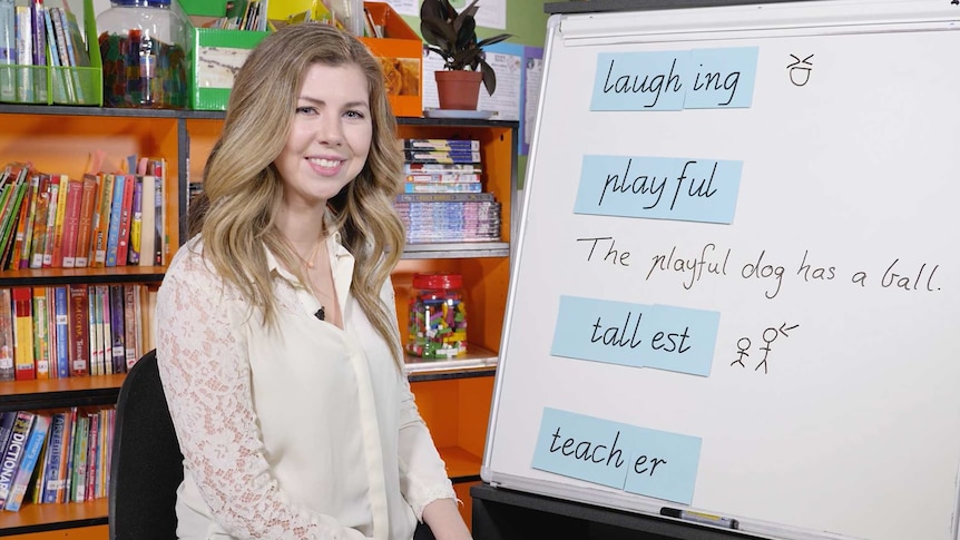 Female teacher sits in front of whiteboard, contains words "laughing", "playful", "tallest", "teacher"
