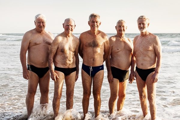 five older men standing in the shallow water ready for a body surf