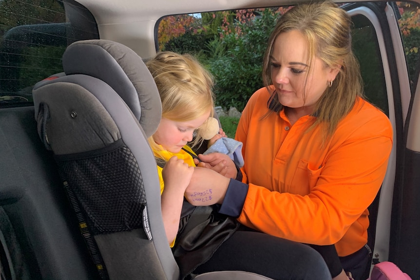 Woman strapping child into car seat. 