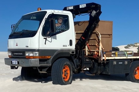 A mitsubishi canter truck sits on a beach in Lancelin with a lady inside. It has orange rims and a container on the tray