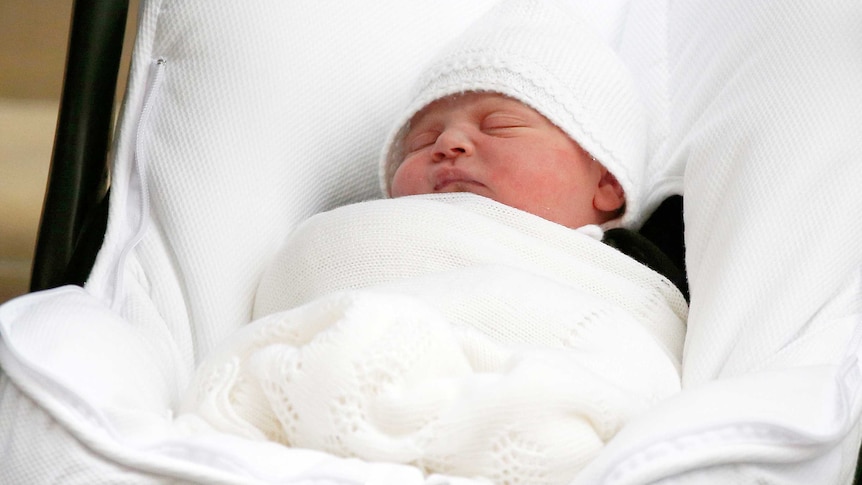 A baby wrapped in white sleeps in a mainly white cot