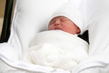 A baby wrapped in white sleeps in a mainly white cot