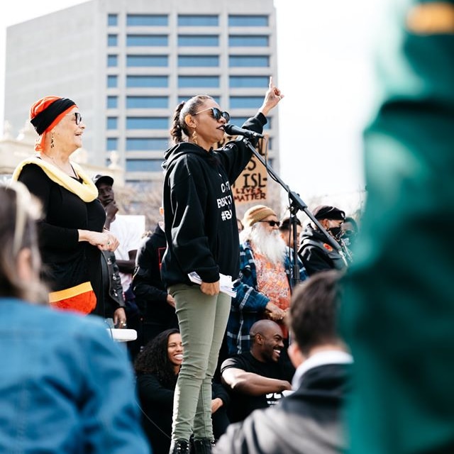 Natasha Wanganeen speaks into a microphone into a large crowd