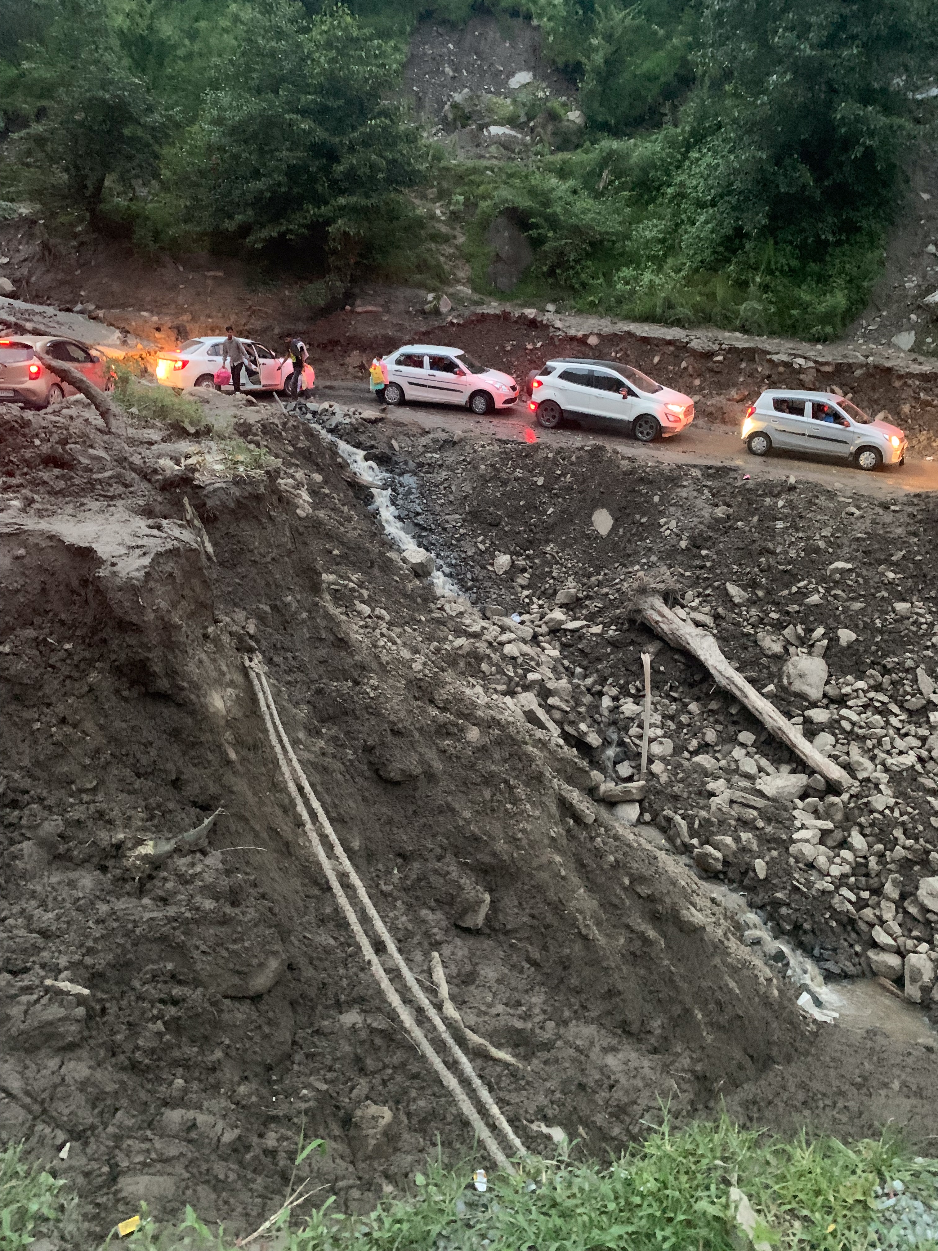 Five cars backed up on a dirt road, a chunk of the mountainside next to them eroded.