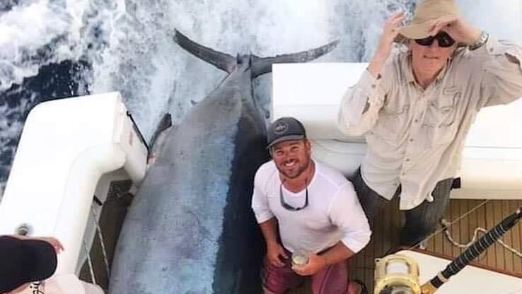 Angler Rob Crane and his crew on board their boat with a large black Marlin laying on the floor after being reeled in.