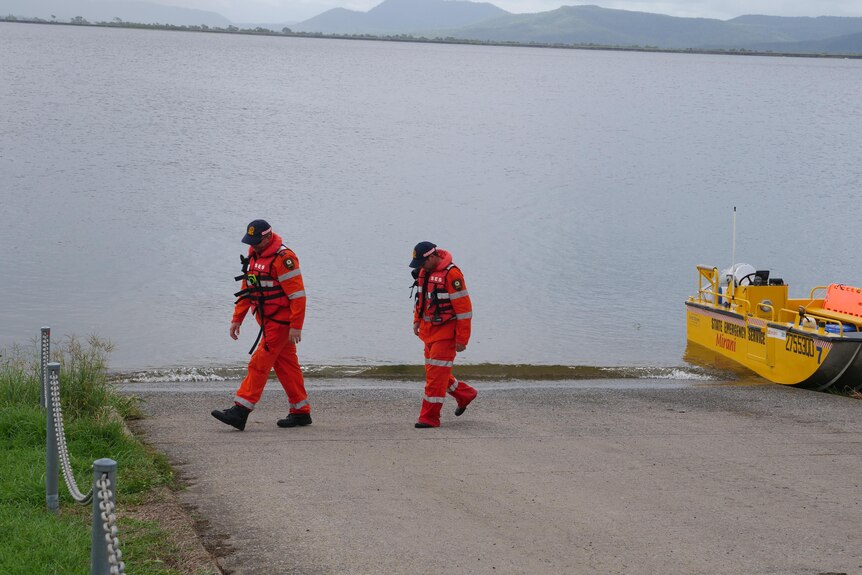 Two SES volunteers in high-vis coveralls walking away from a boat parked at boat ramp.