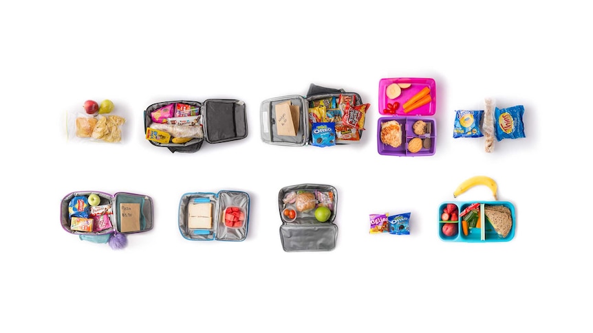Nine different children's open lunch boxes, showing sandwiches, chocolates, chips, biscuits and fruit, on a white background.