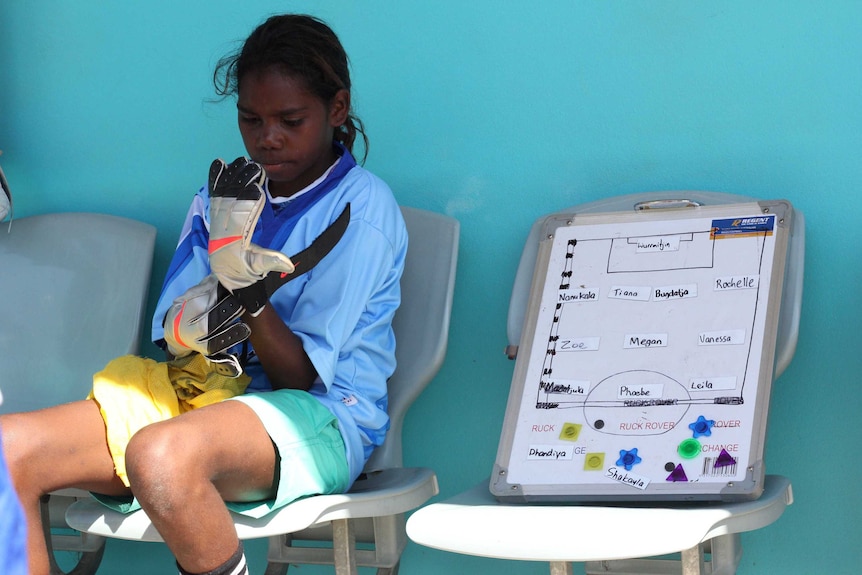 A young girl puts on a soccer glove.