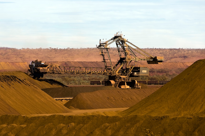 A very large mining machine works in an area of red dirt. 