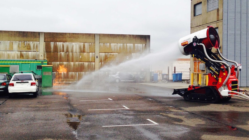 A fire fighting robot sprays a jet of water onto a fire in a car park.