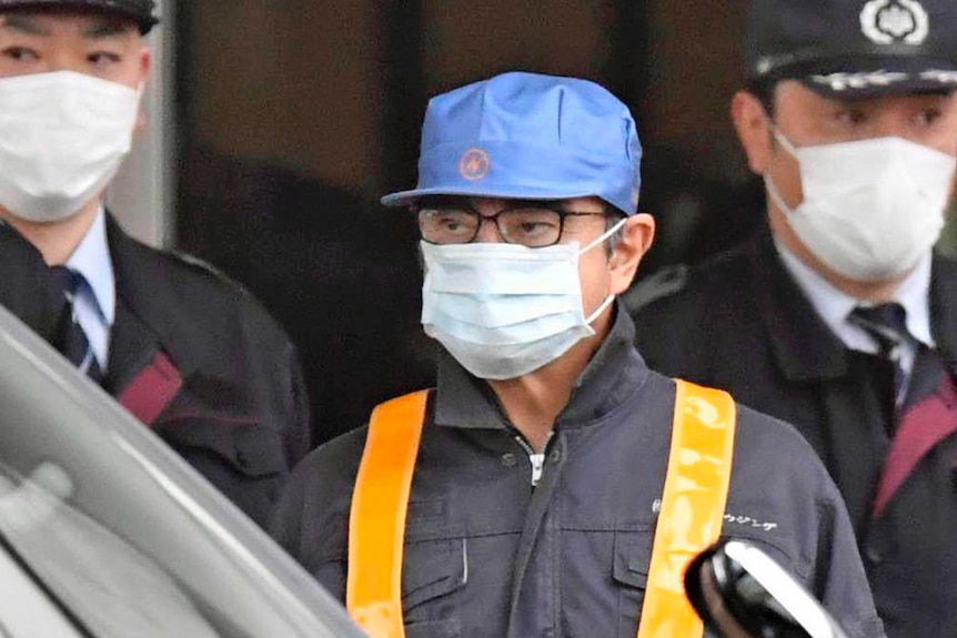 Carlos Ghosn wears a blue cap with an electric bolt on it and a mask as he leaves a detention centre.