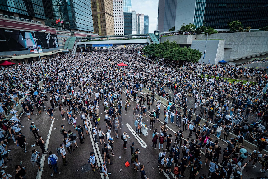 A view from above of thousands of people on the street with large buildings in the background.