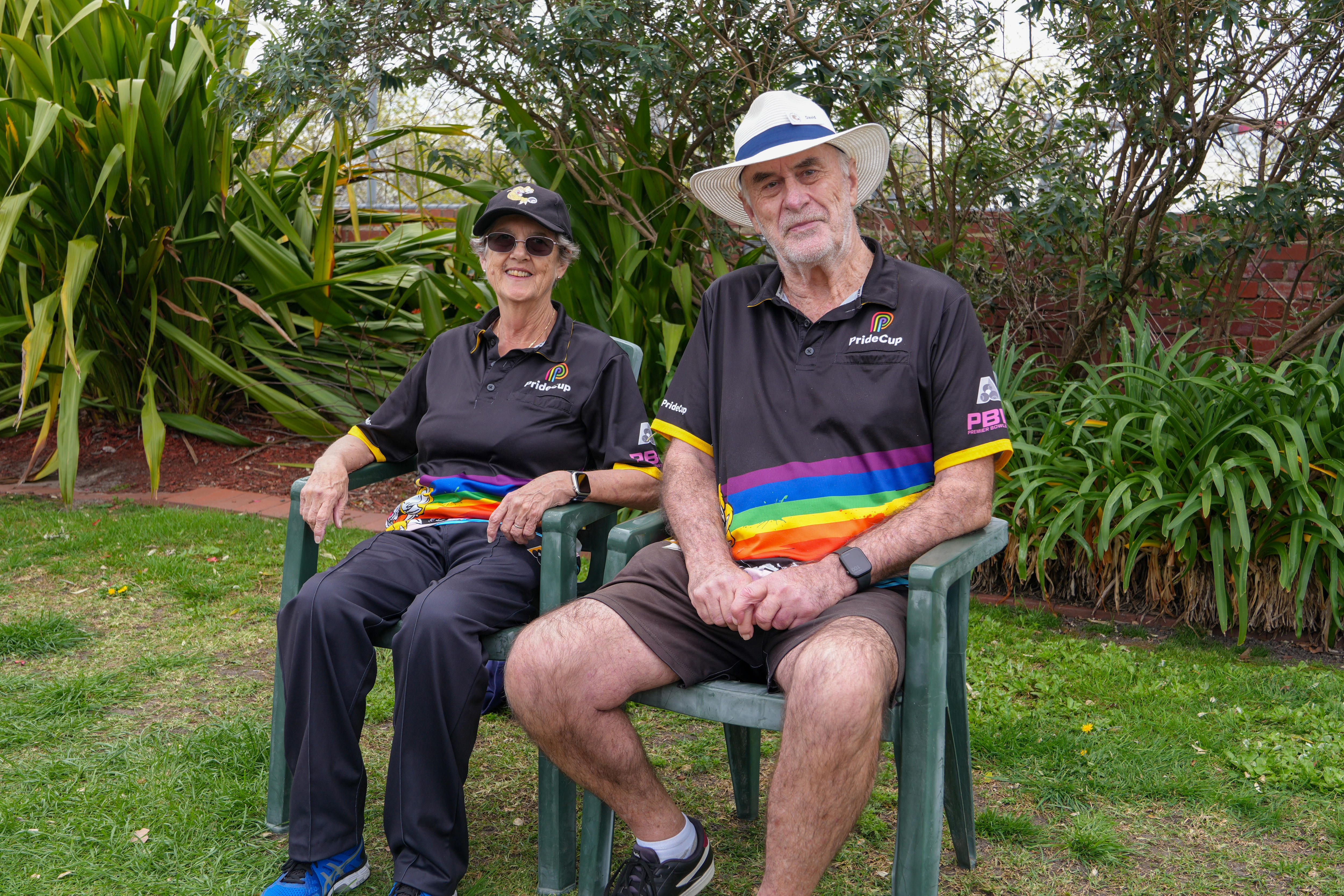 Dois membros do gramado sentam-se em cadeiras de gramado com camisas do orgulho listradas com arco-íris.