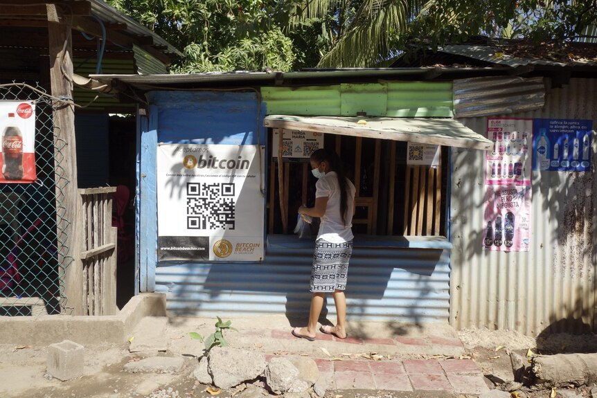 A woman stands next to a street stall showing QR code for bitcoin