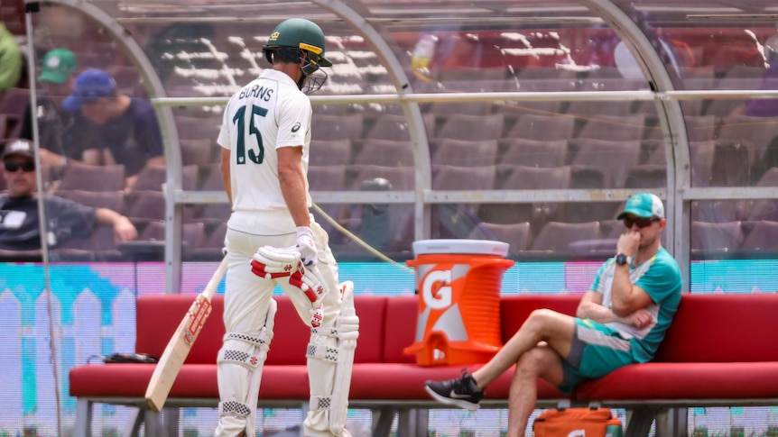 Australia A batsman Joe Burns walks off the ground after being dismissed in a tour match. Assistant coach Chris Rogers looks on.