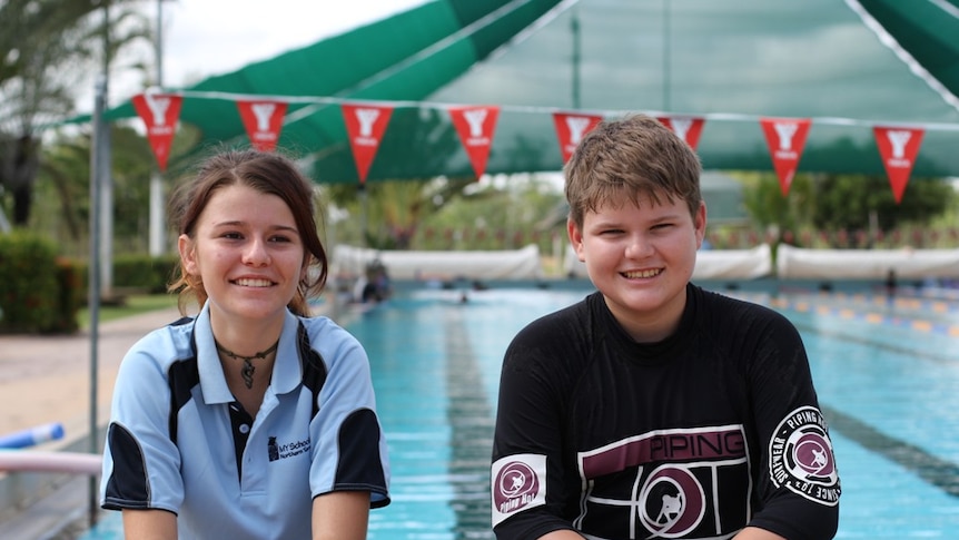 two students sitting on the edge of a swimming pool