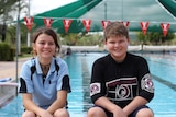 two students sitting on the edge of a swimming pool