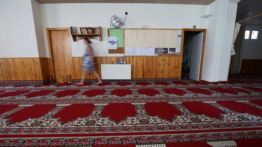A woman walks past a door in the carpeted  mosque