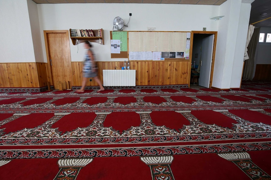 A woman walks past a door in the carpeted  mosque