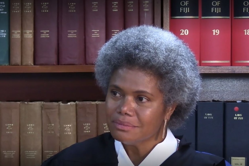 Head shot of woman with grey afro sitting infront of law books lining the book shelf.  