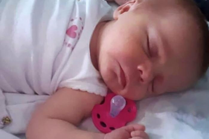A baby sleeping with a dummy lying just next to her cheek. 