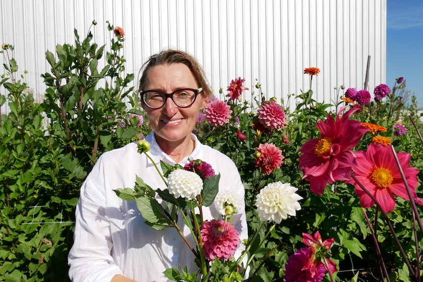 Elena rogers standing in front of pink flower crop holding a bunch of dahlia flowers. 