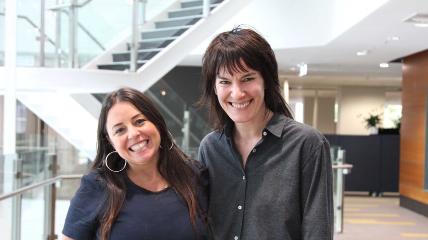 Two women, Myf Warhurst and Jen Cloher, smile looking at the camera in the ABC foyer