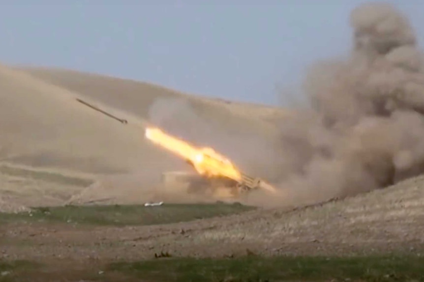 A rocket launches from a missile system that sits in the low point of a shallow, sparse and rocky valley