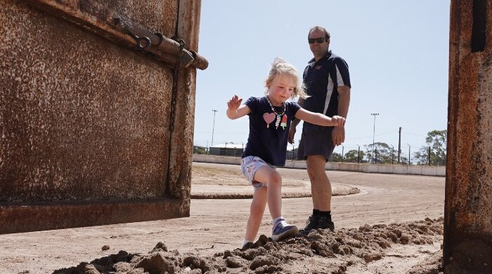 A man watches his young daughter play on a part of a speedway racing track