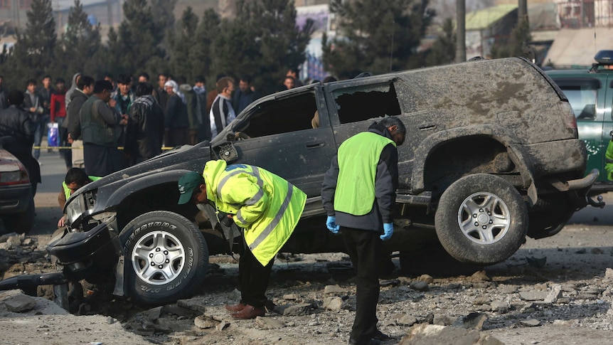 Afghan security personnel inspect the site of a roadside bomb blast in Kabul, Afghanistan