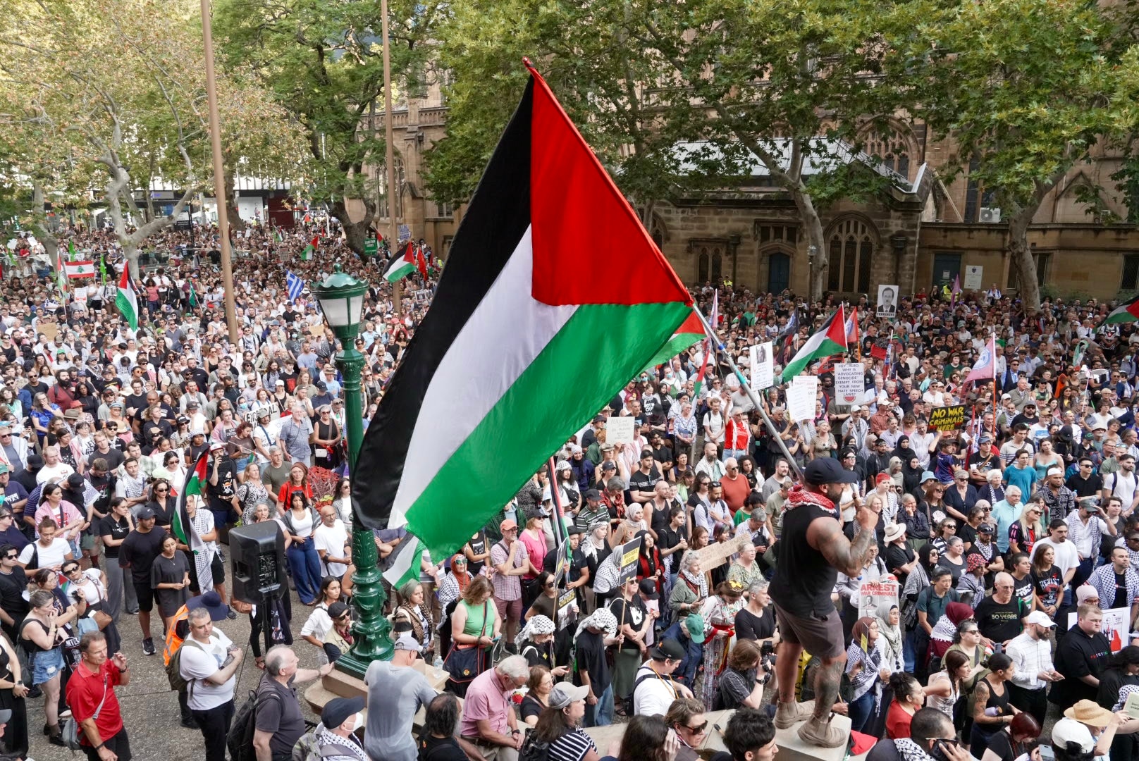 Gran bandera palestina verde, roja, blanca y negra sostenida por un hombre rodeado por una multitud de personas.